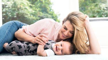 A mum lying on the floor with her baby, smiling and happy, knowing she can breastfeed him without having to remove her PurelanTM 100 lanolin cream.